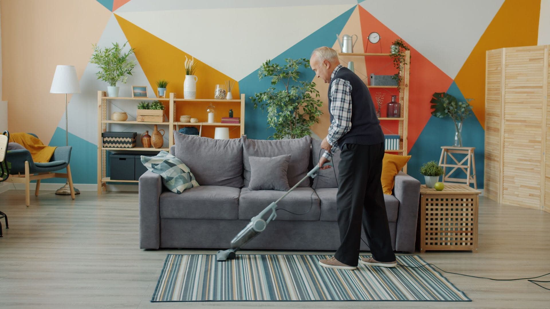 Man vacuuming a striped rug in a colourful living room