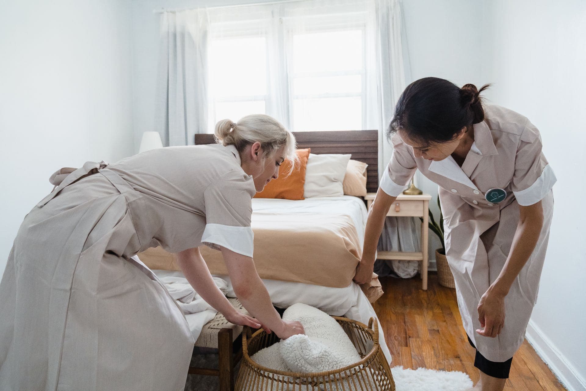 Two housekeepers changing bedding in a bright bedroom